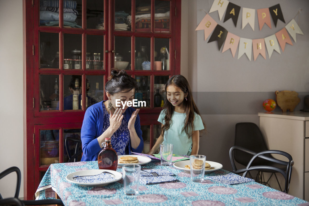 Surprised mother looking at pancakes made by daughter on birthday