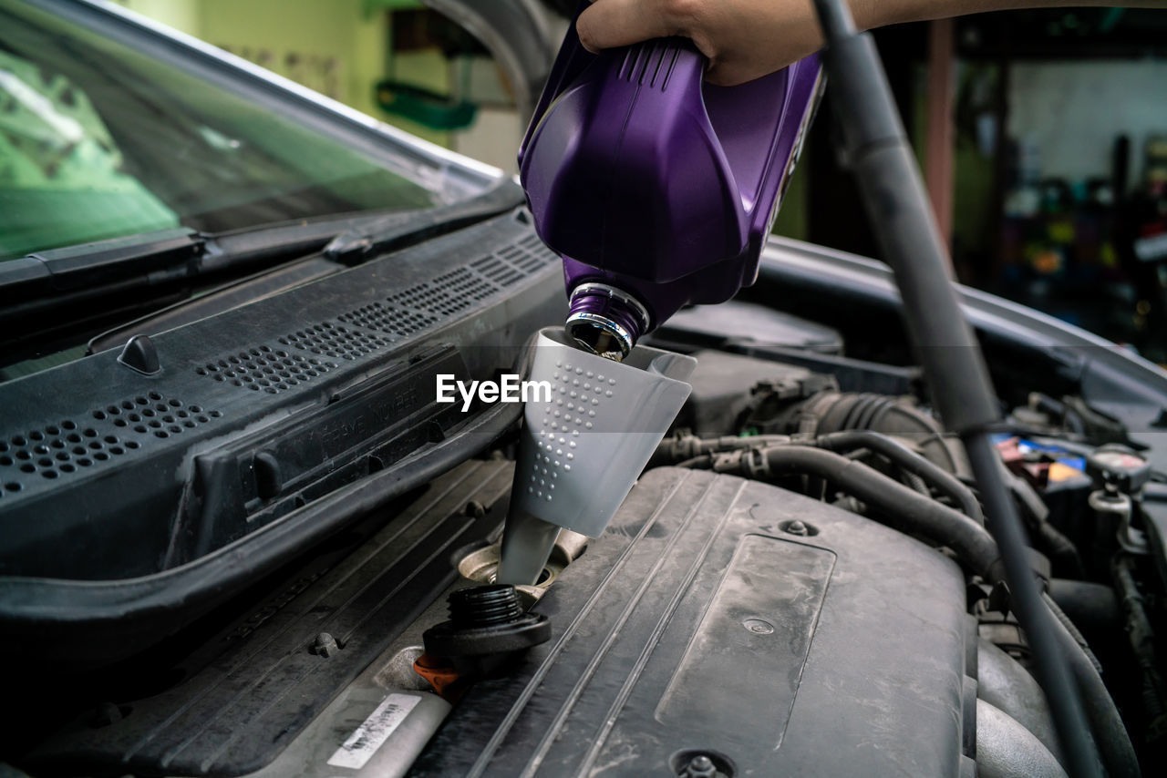 Cropped hand of woman pouring motor oil in garage