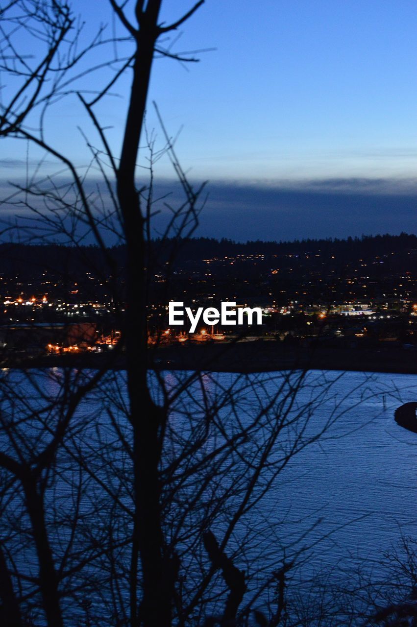 SILHOUETTE OF BARE TREES BY RIVER AGAINST SKY