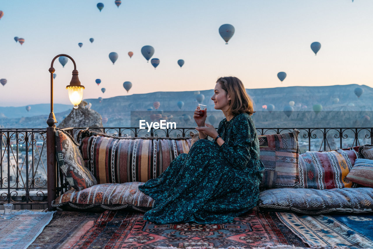 Woman drinking early morning tea with hot air balloons in cappadocia