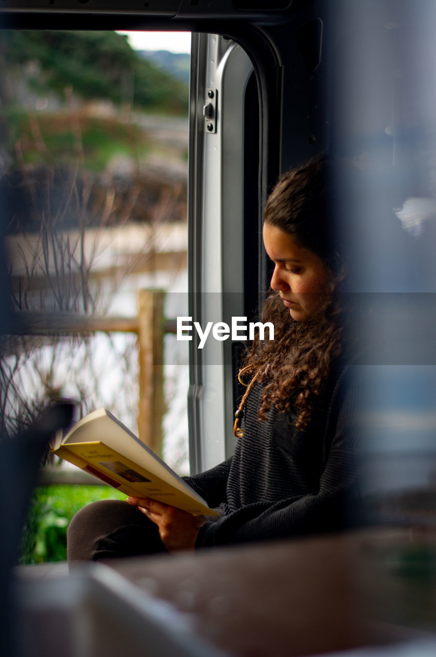 Woman reading book while sitting by window at home