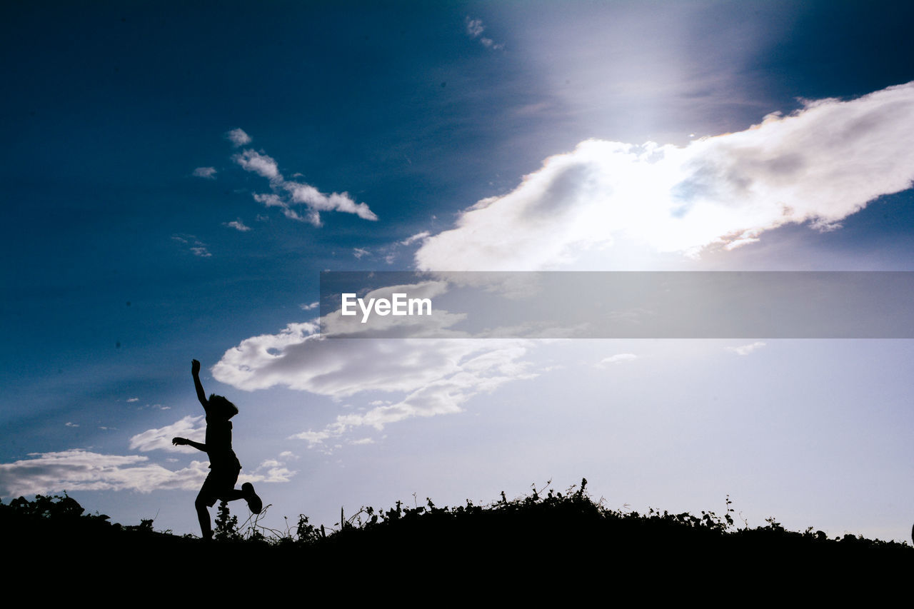 Low angle view of silhouette boy jumping against blue sky