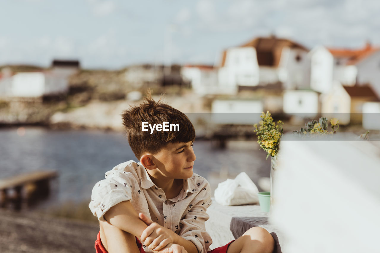 Contemplating boy looking away while sitting outdoors during sunny day