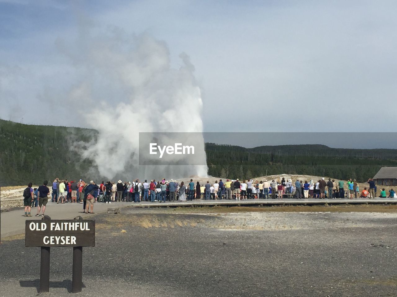 Tourist visiting old faithful geyser at yellowstone national park against sky