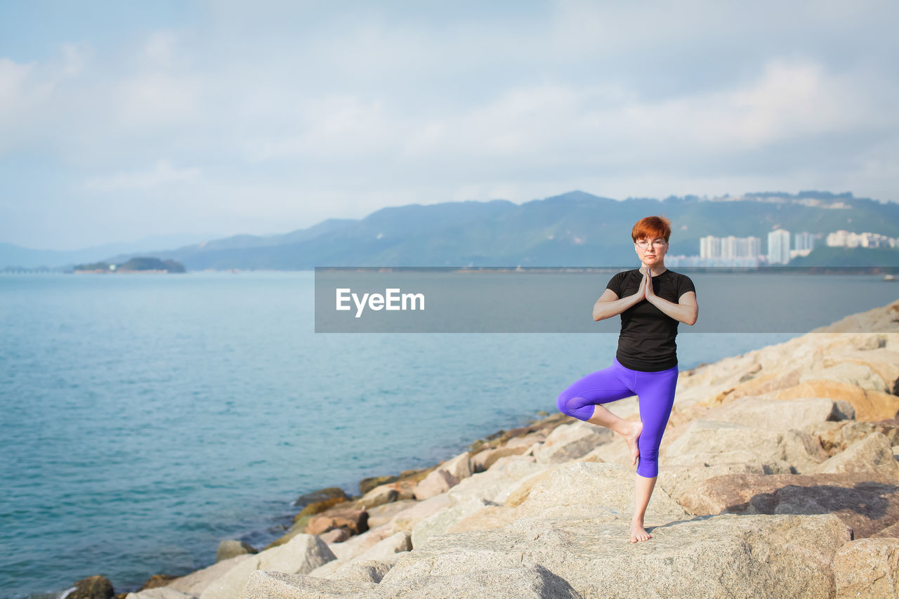 Full length of mature woman practicing yoga on rocks at beach