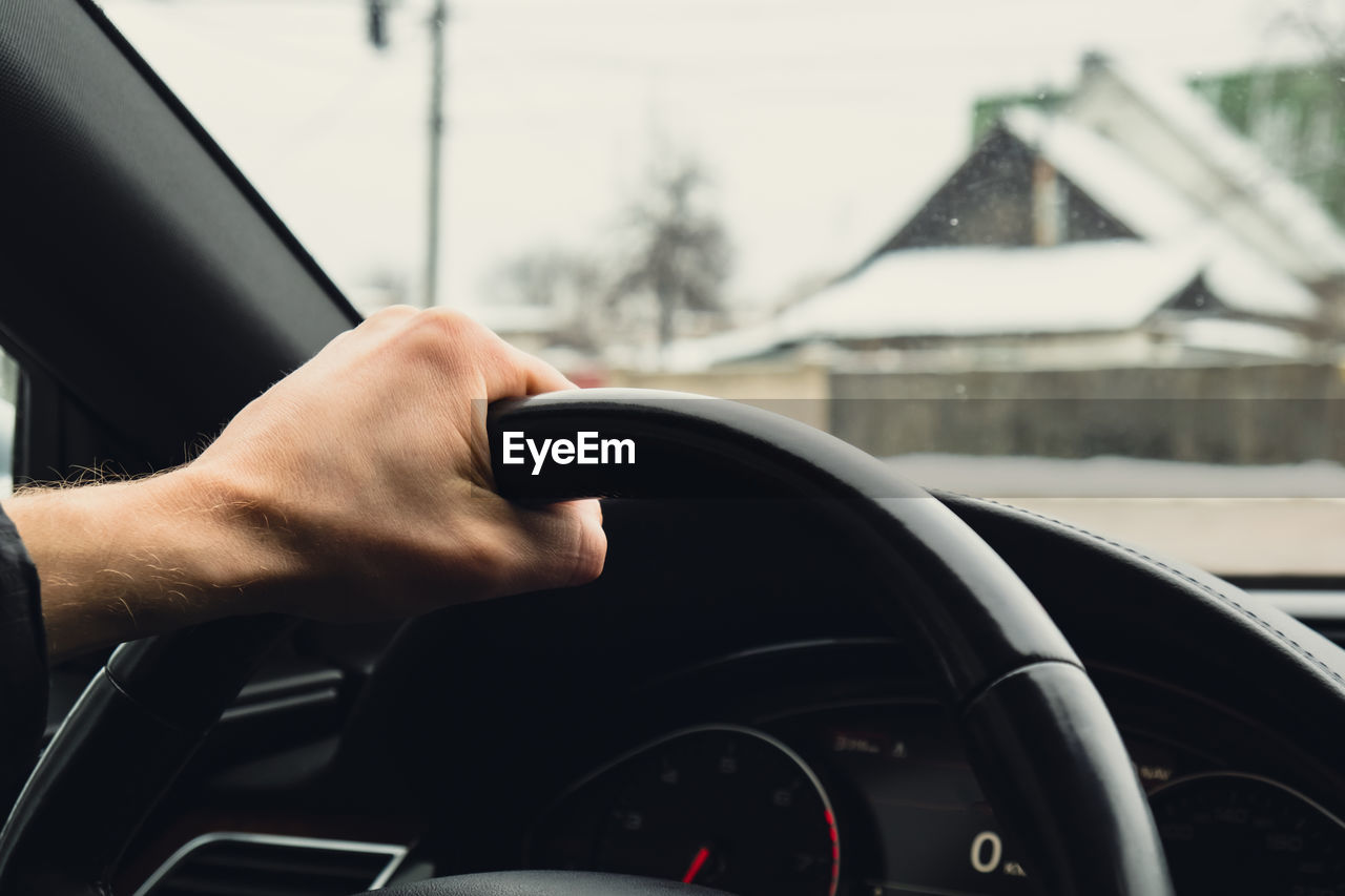 Selective focus man's hand on steering wheel, driving car in winter background. travel background
