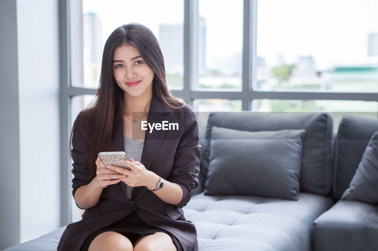 Portrait of beautiful businesswoman using smart phone while sitting on sofa in office