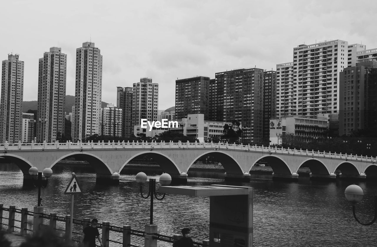 Bridge over river by buildings against sky in city