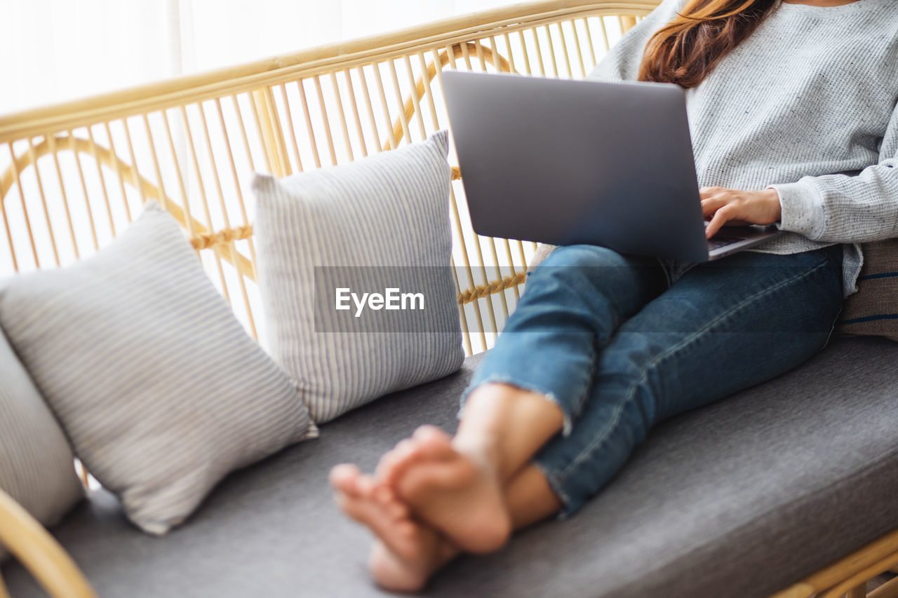 midsection of man using laptop while sitting on sofa at home