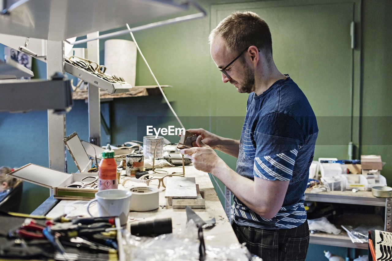 Side view of male owner working at desk in eyewear workshop
