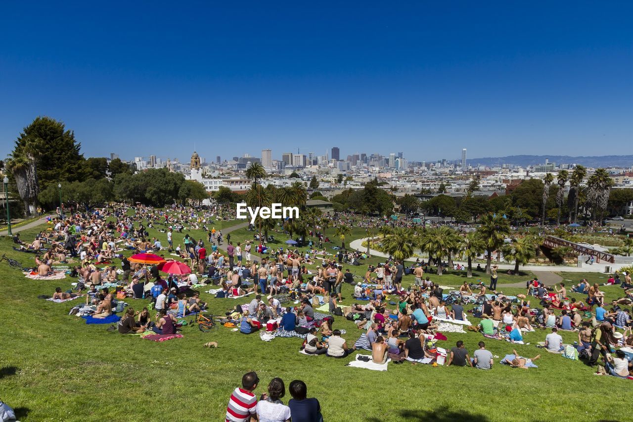 Large group of people sitting on lawn against clear blue sky