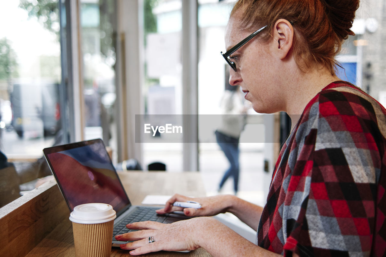 Woman wearing eyeglasses using laptop at cafe