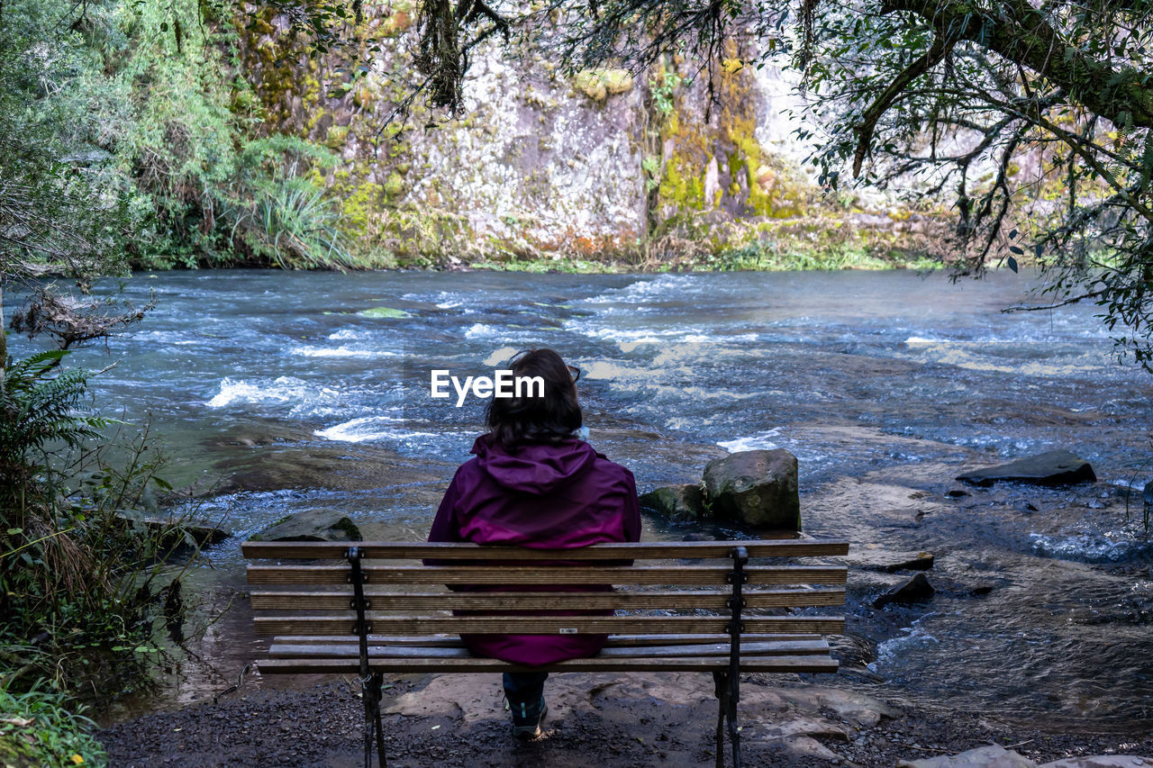 REAR VIEW OF GIRL SITTING ON BENCH IN WATER