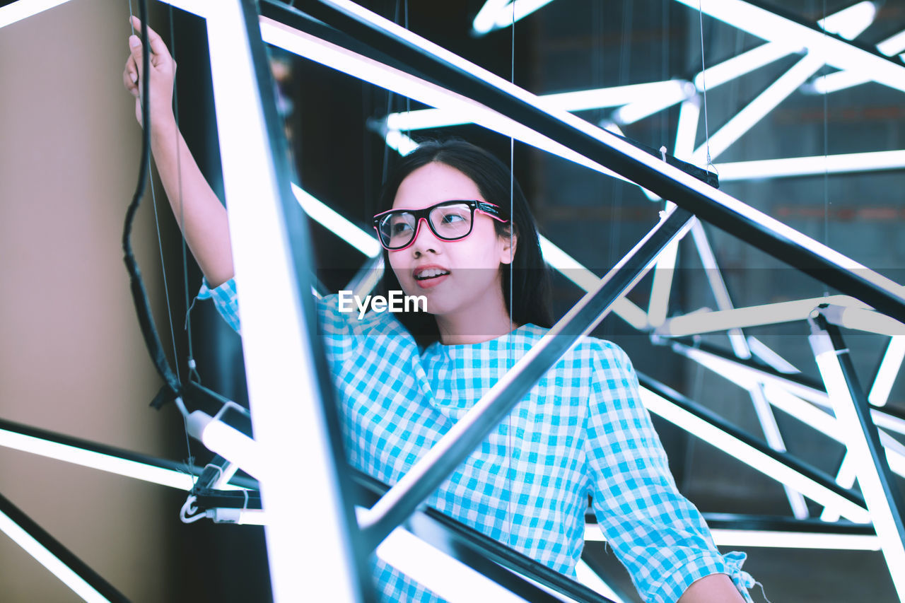 Low angle view of beautiful young woman standing amidst illuminated fluorescent lights