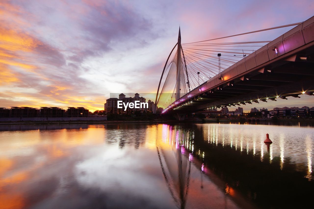 Bridge over river in city against sky during sunset