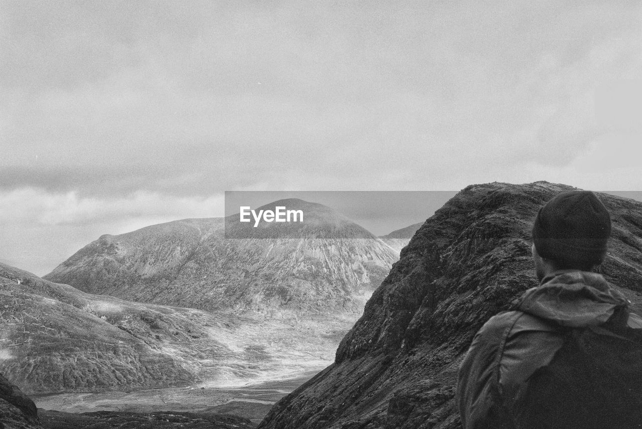 Rear view of man standing on mountain against sky