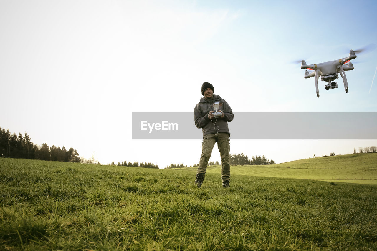 Man on a meadow flying drone while his dog watching