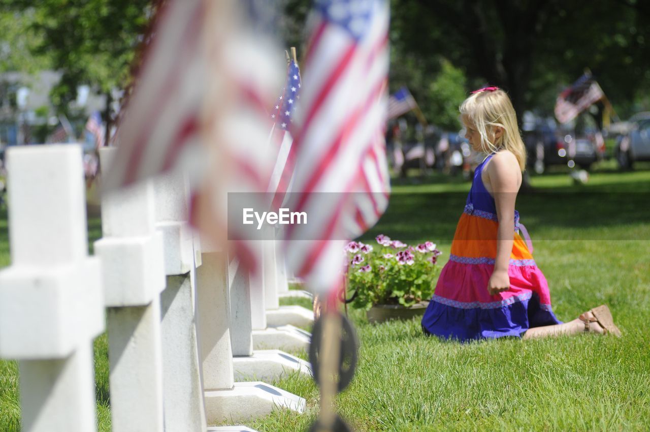 Side view of girl kneeling by tombstones in cemetery