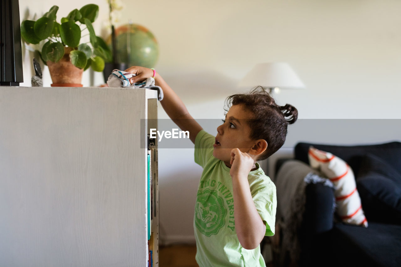 Side view of boy cleaning cabinet with napkin at home