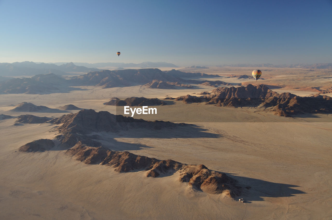 Scenic view of namib desert against sky, with hot air balloons