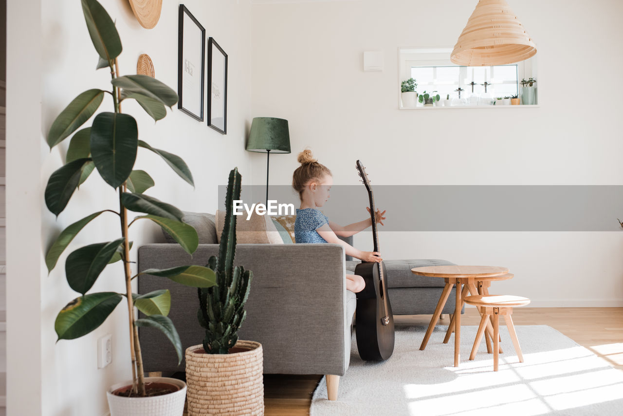 Young girl holding a guitar, musical instrument whilst sat at home