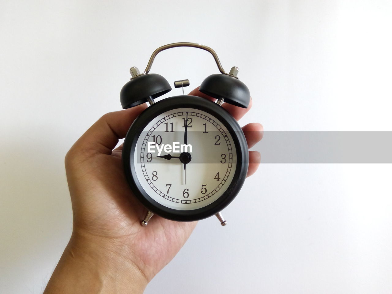 Close-up of hand holding alarm clock against white wall