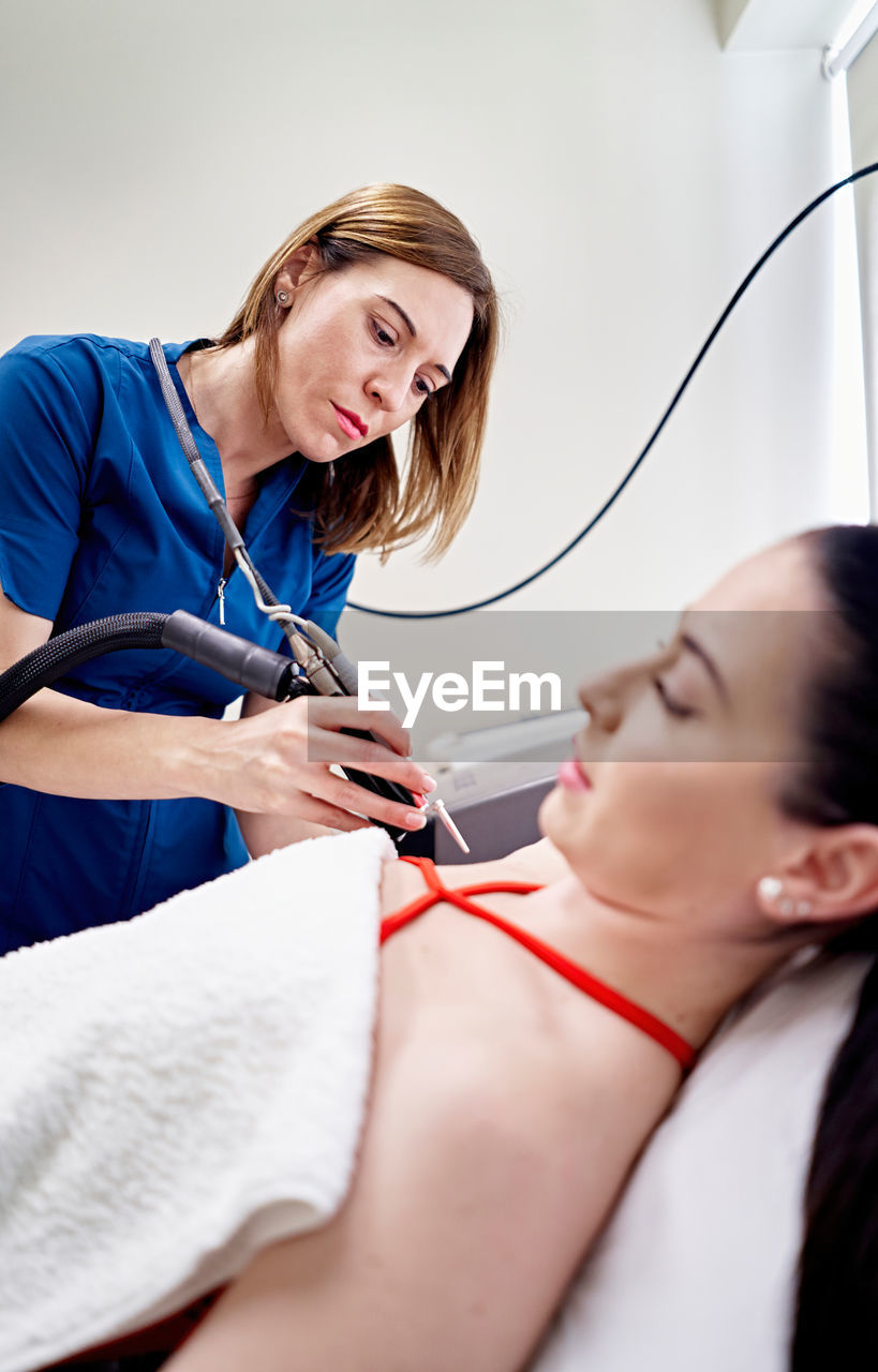 Beautician removing hair from armpit of female customer during laser epilation procedure in aesthetic clinic