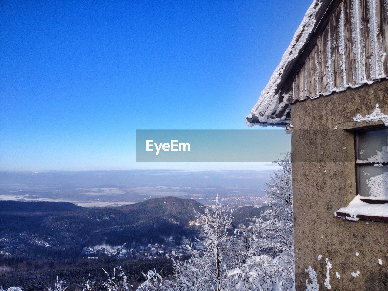 Wooden house on mountain against clear blue sky during winter