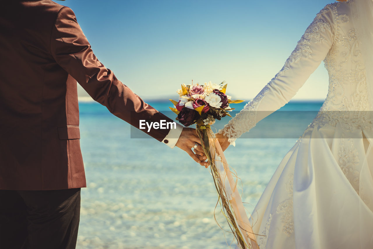 Low angle view of bride and groom standing against sea