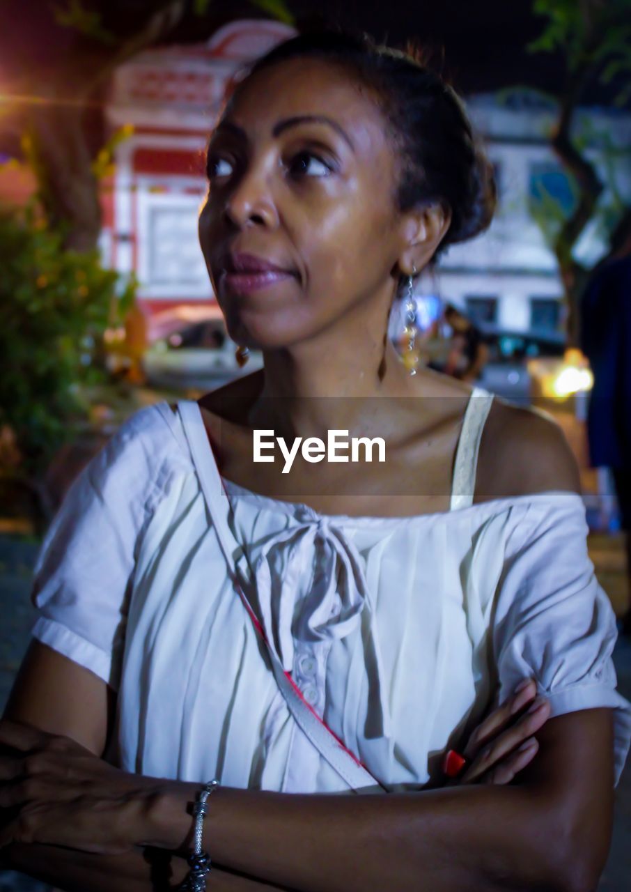 Woman looking away while standing outdoors at night