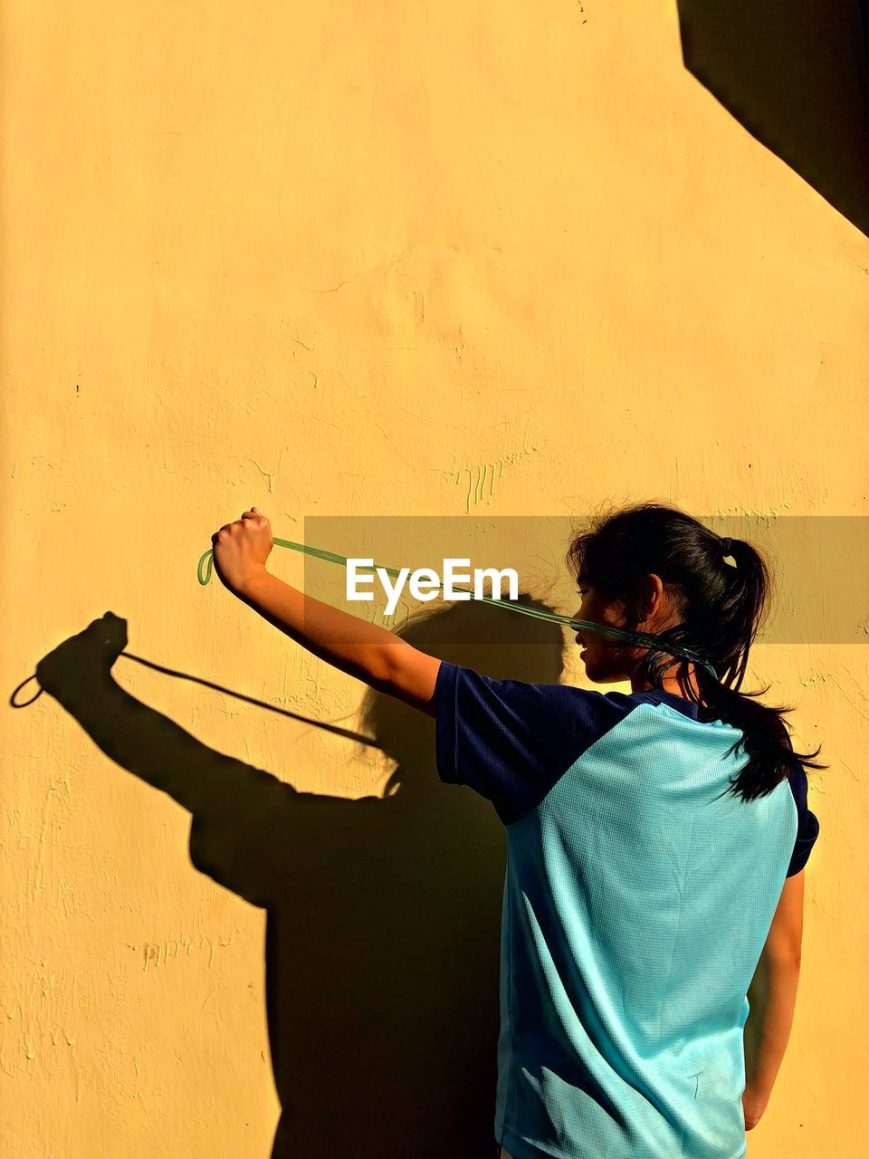 Shadow of girl with skipping rope on yellow wall