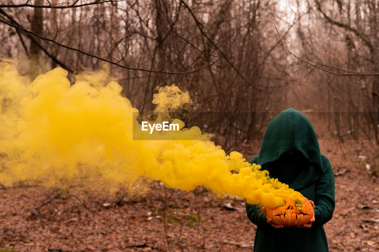 Woman holding smoke emitting pumpkin in forest