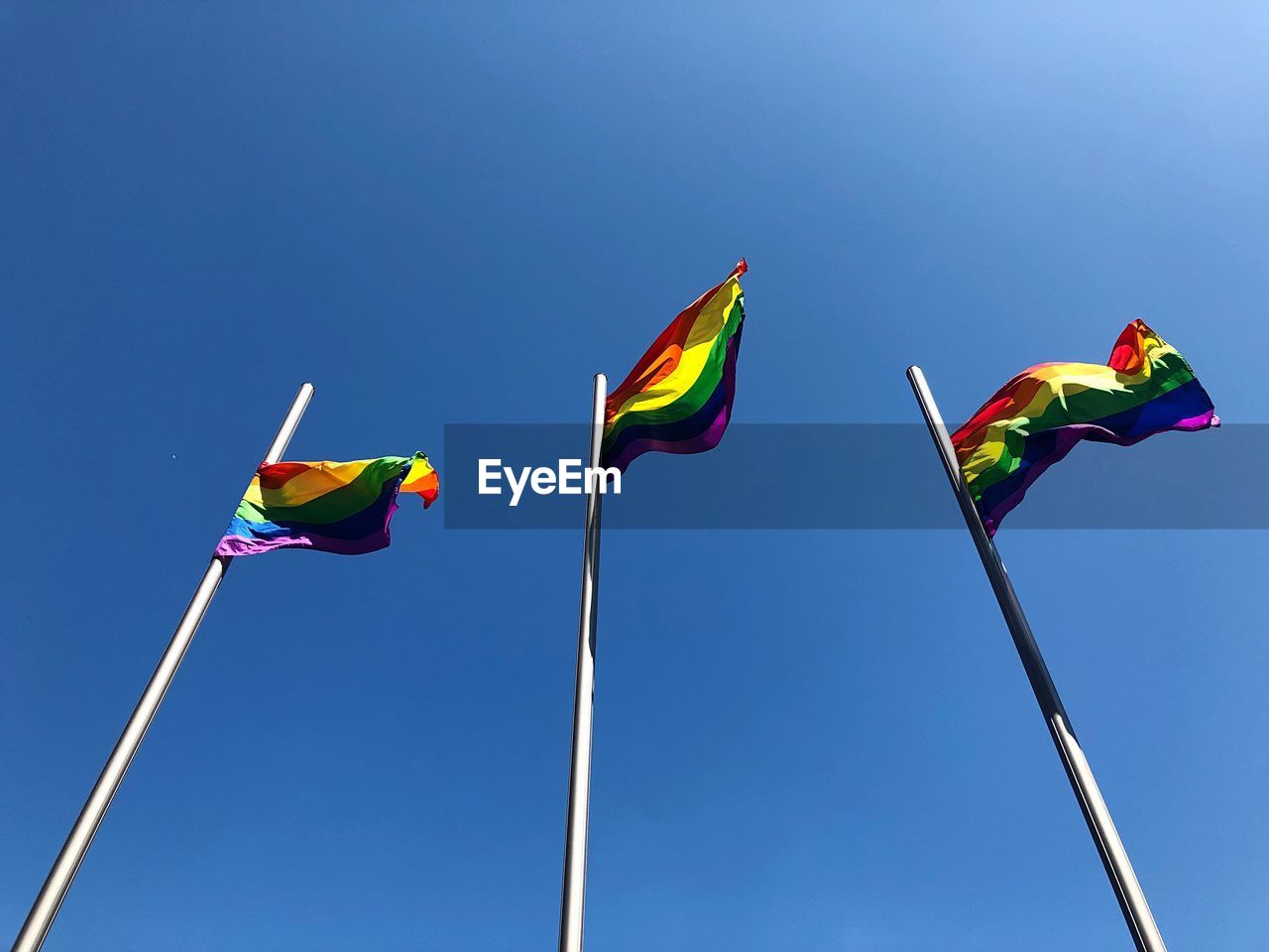 Low angle view of rainbow flags against clear blue sky