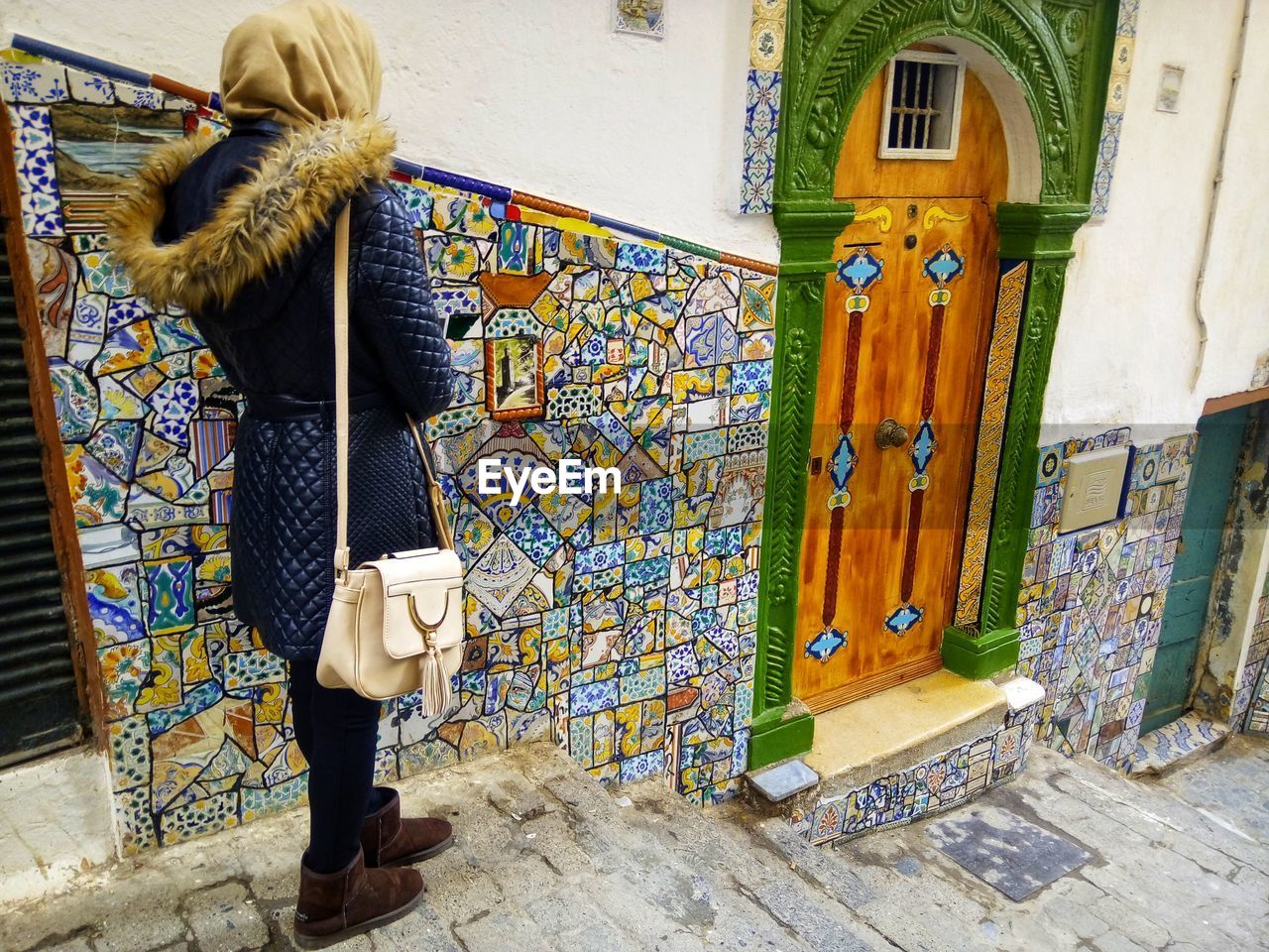 REAR VIEW OF WOMAN STANDING AGAINST WALL