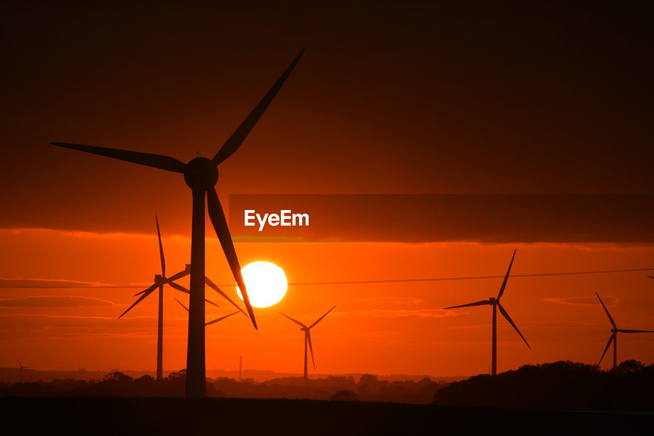 A bright red sunset through wind turbines