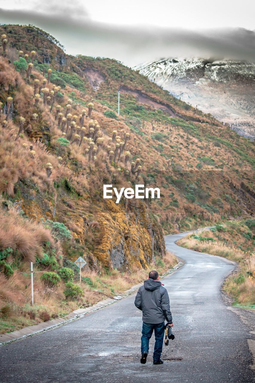 Rear view of man walking on road against mountain