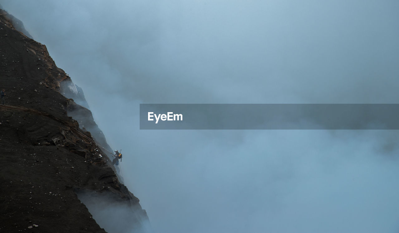 High angle view of hiker climbing on mountain during foggy weather
