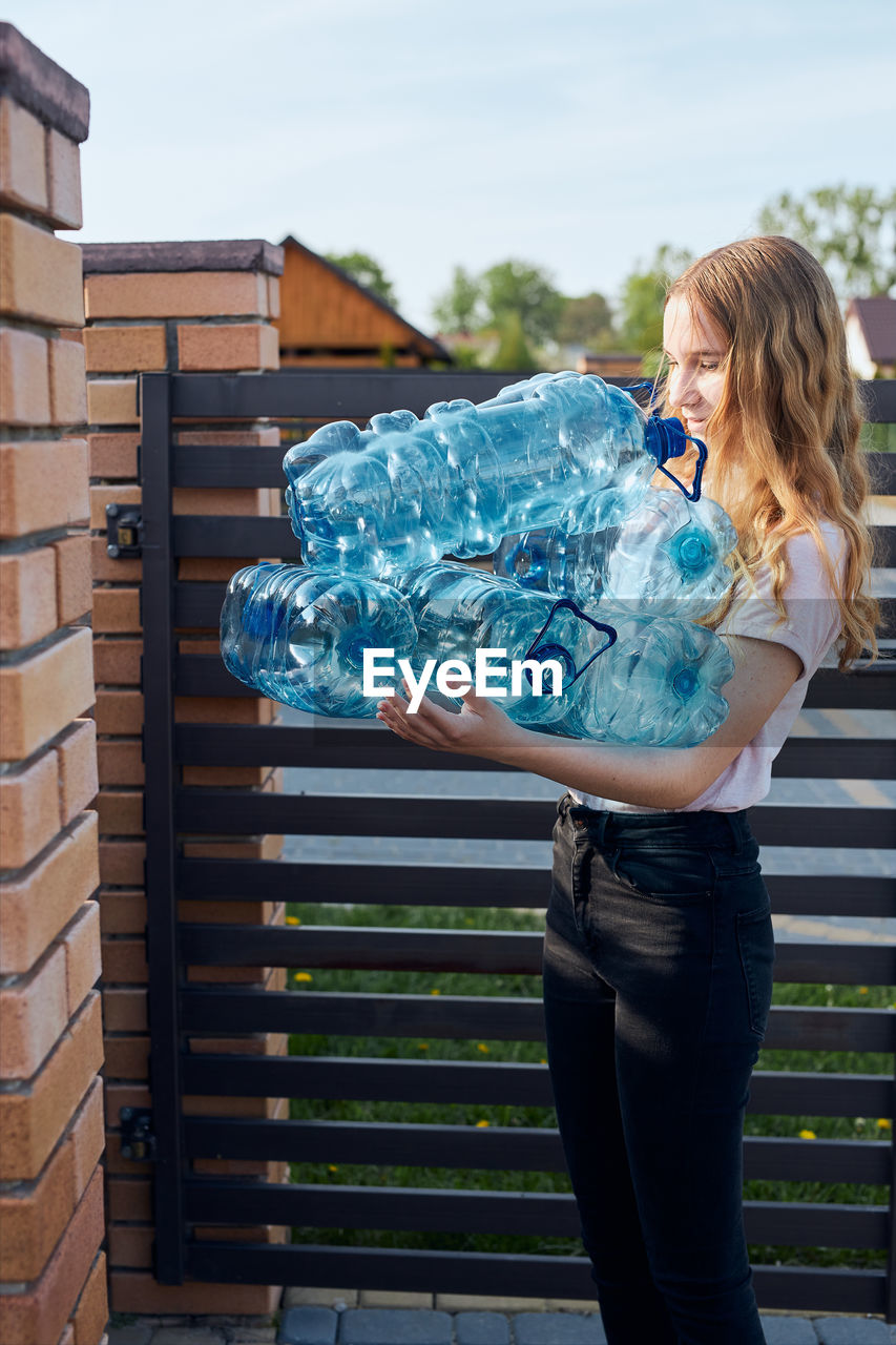 Girl holding blue empty bottle while standing outdoors