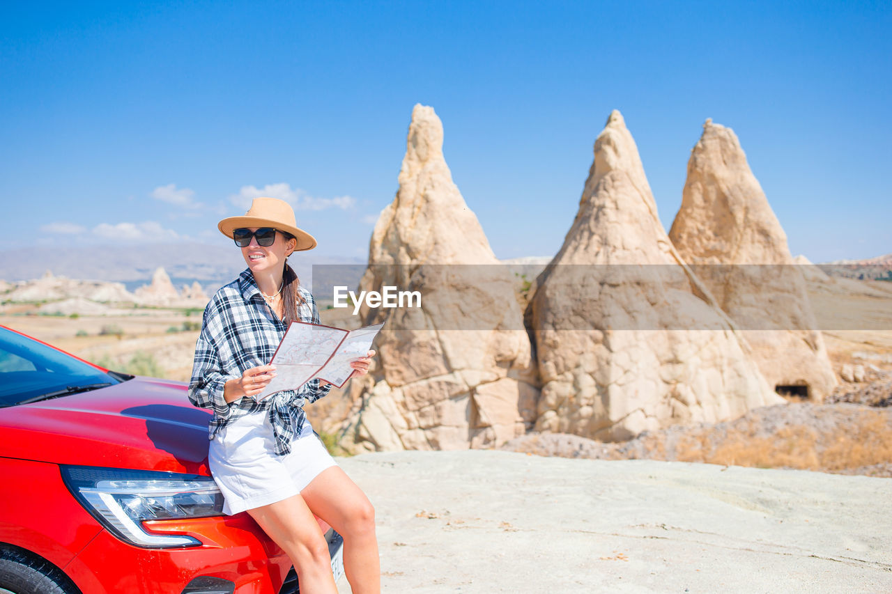 side view of woman sitting on rock against clear sky