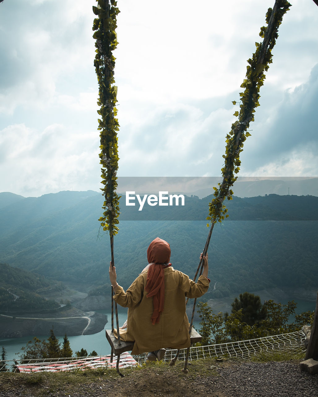 Rear view of woman sitting on swing against mountains