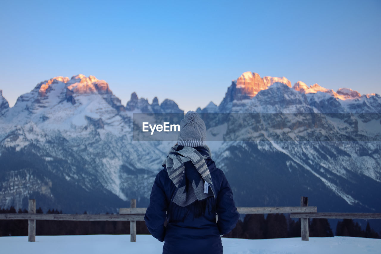 Woman standing on snowcapped field against clear blue sky