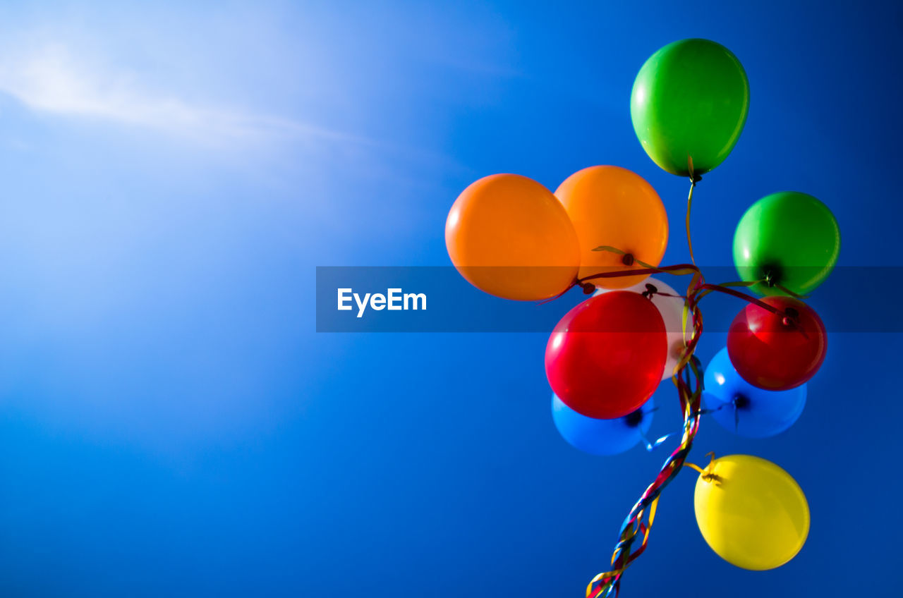 Low angle view of colorful helium balloons against sky