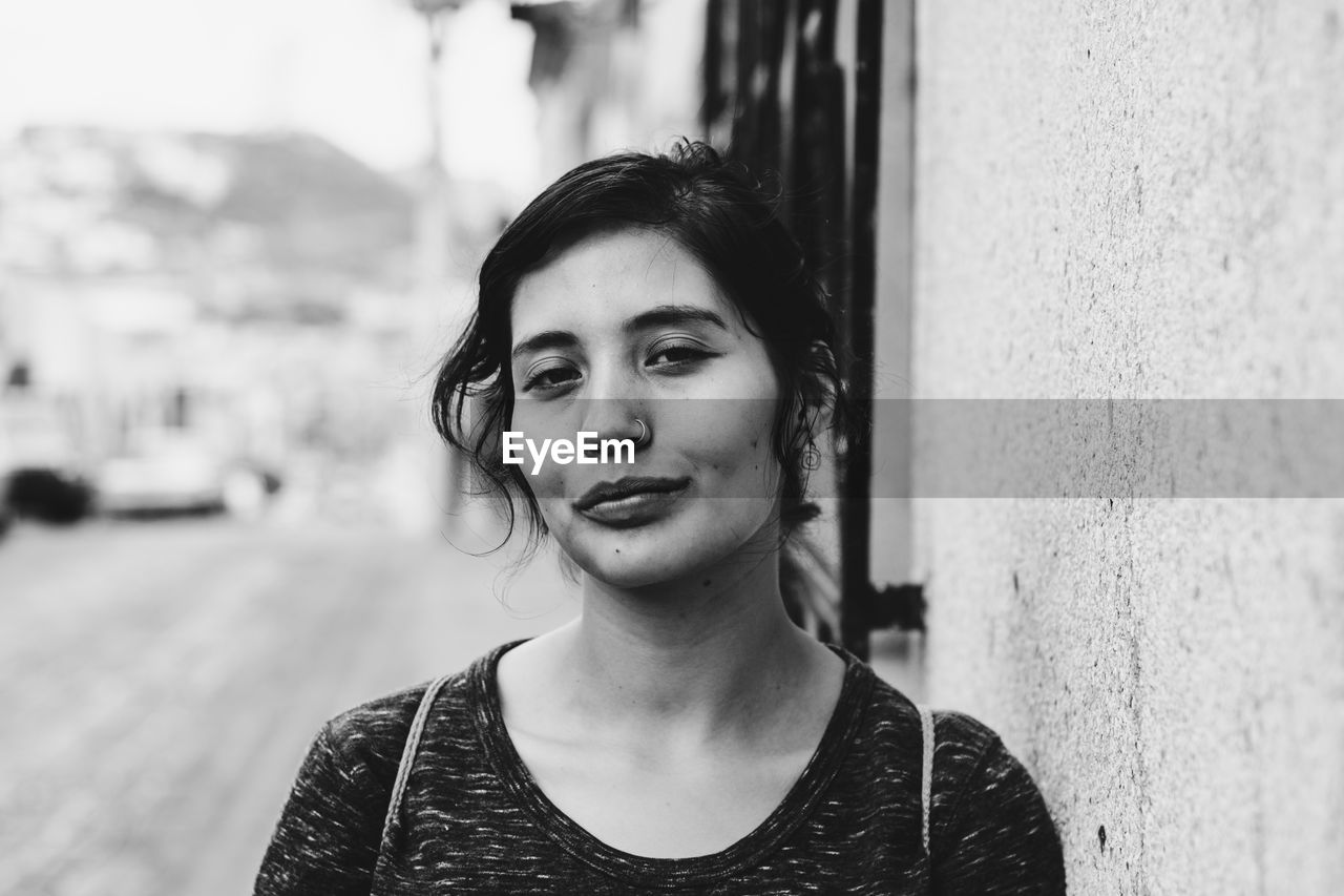 Close-up portrait of beautiful woman standing by wall in city