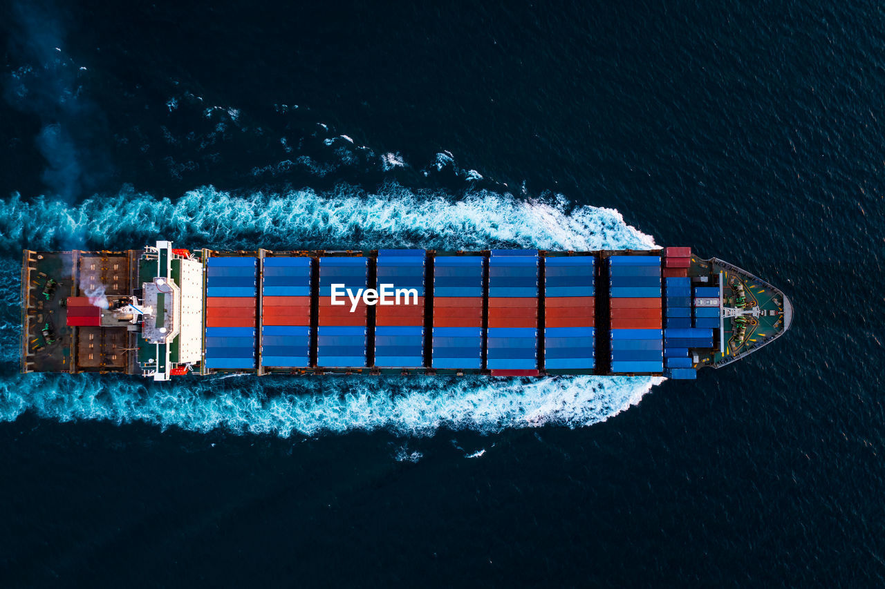 Aerial top view full speed container ship in the deep blue sea for cargo logistics import and export 