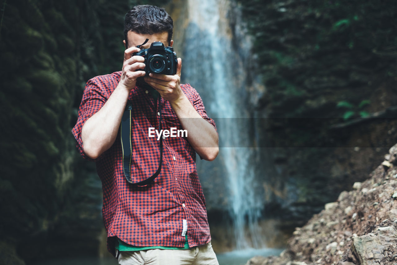 Man photographing through digital camera against waterfall