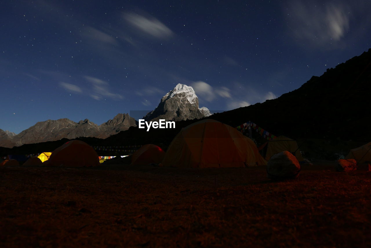 Tents by rocky mountains against sky at night