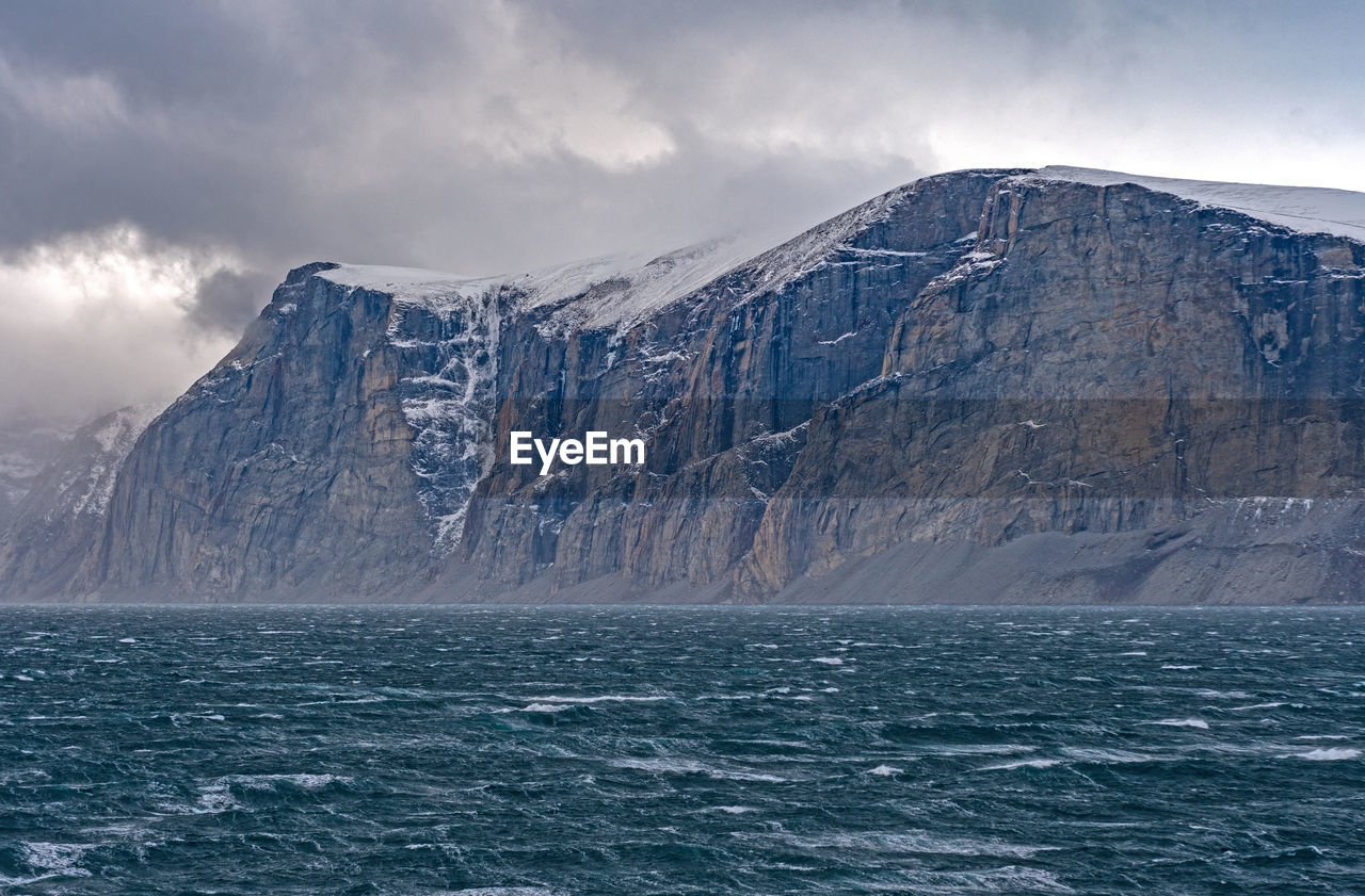 Dramatic cliffs above storm tossed seas in the sam ford fjord on baffin island in nunavut, canada