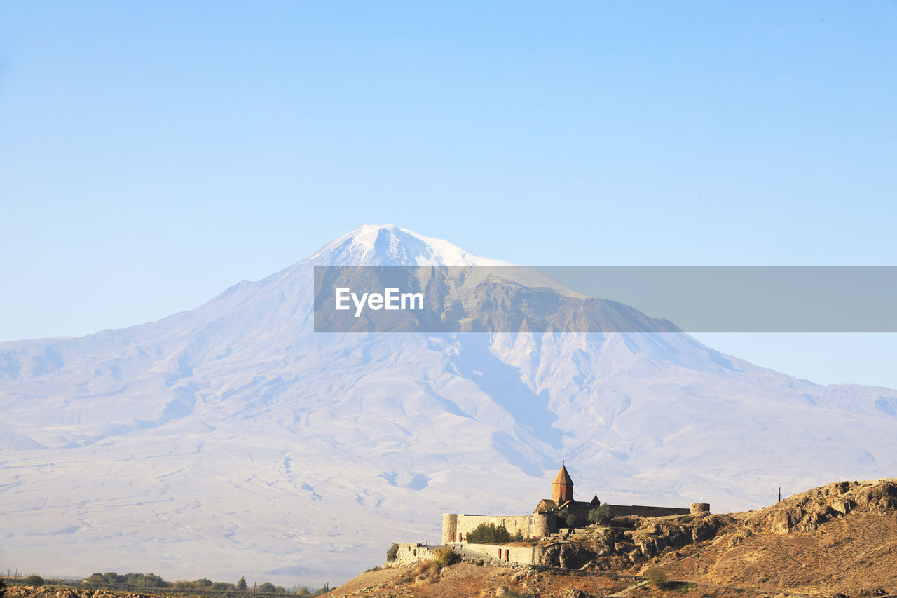 Scenic view of built structure against snowcapped mountain and sky