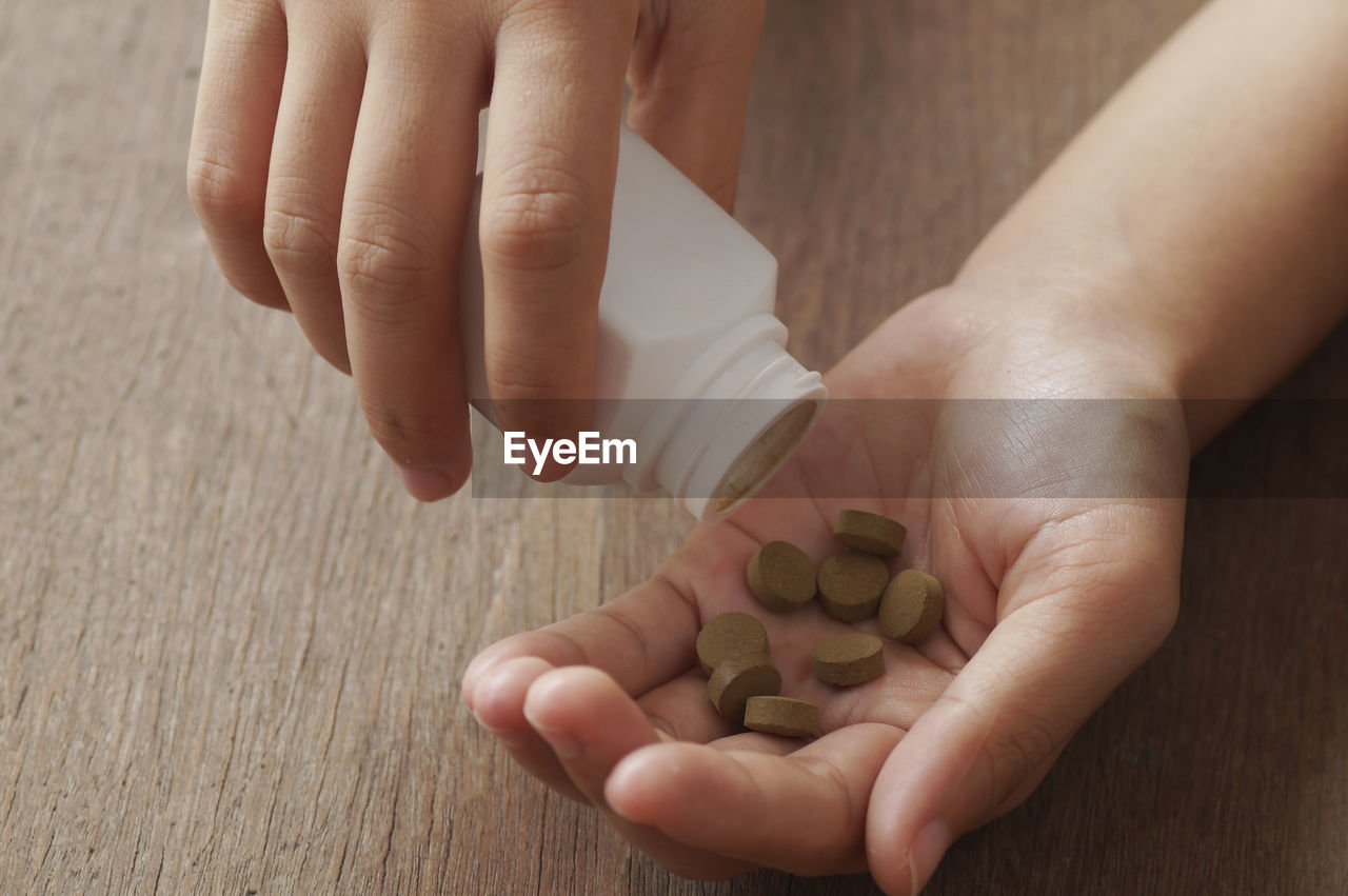 Cropped hands of person holding medicine bottle on wooden table