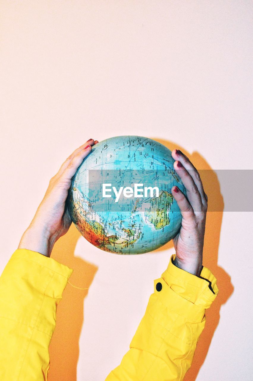 Cropped hands holding globe against wall